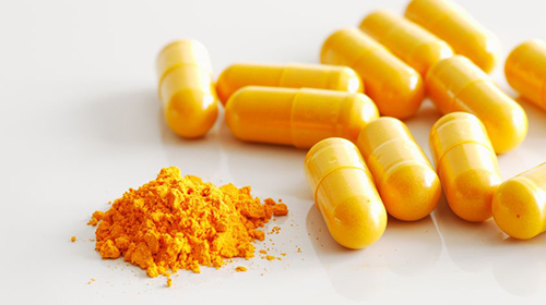 21649244 - a handful of turmeric capsules on white reflective ceramic surface, with the contents of one spilled open
